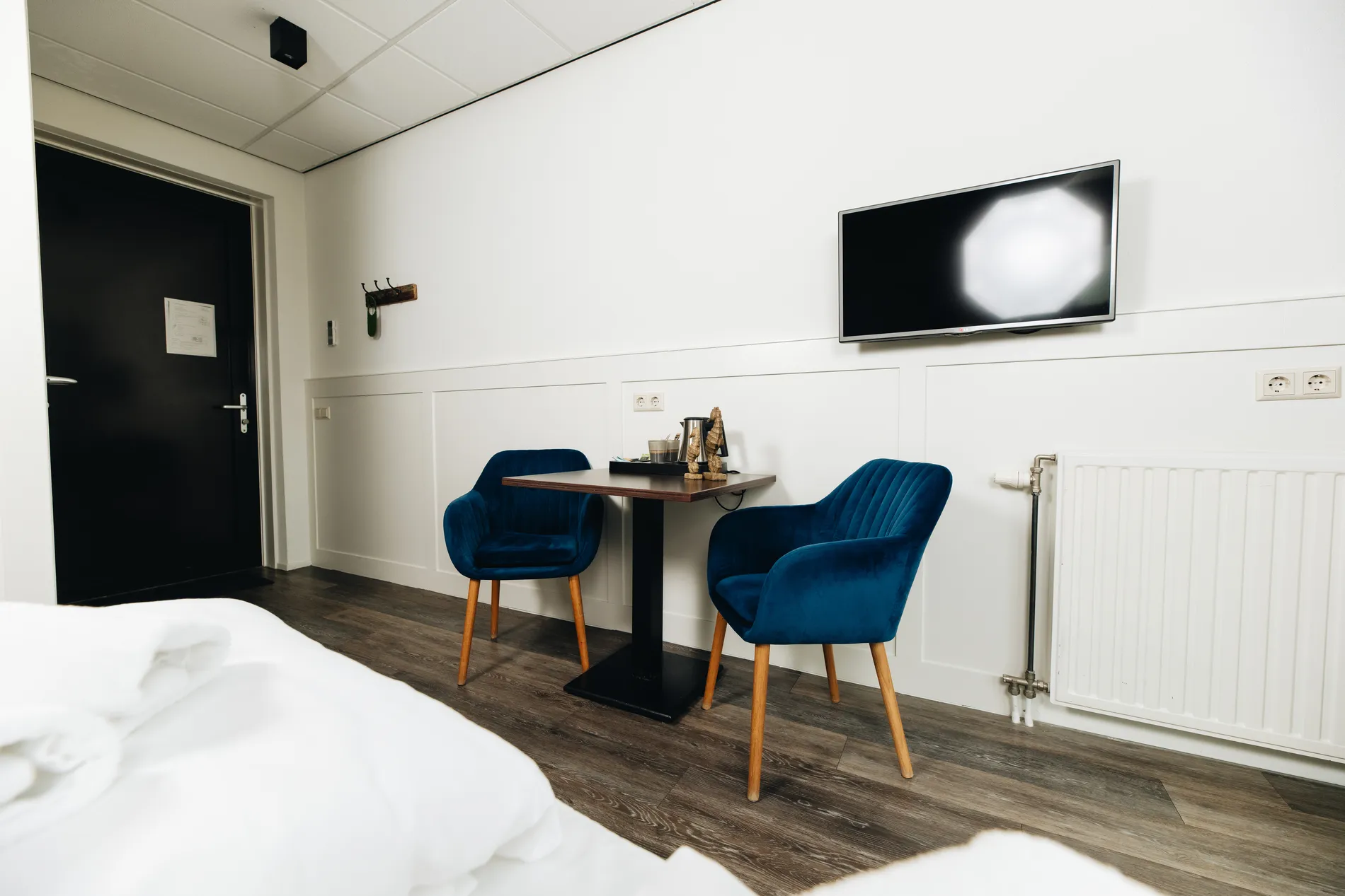 Comfortabel zitgedeelte in de hotelkamer met twee blauwe fluwelen stoelen, een moderne tafel en koffiefaciliteiten bij Resort Land & Zee.
